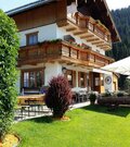 Alpines Gasthaus mit Holzfassade, Balkonen und einer Außenterrasse mit Sonnenschirmen vor bewaldetem Berg.