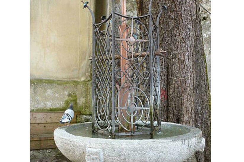 Brunnen bei der Katharinenkirche Ein dekorativer Brunnen aus Stein mit einem kunstvollen Gitter. Neben dem Brunnen sitzt eine Taube.