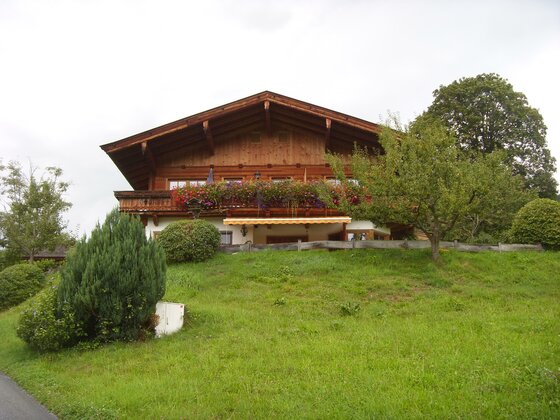 Alpines Holzhaus mit blumengeschmücktem Balkon auf einer grünen Wiese.