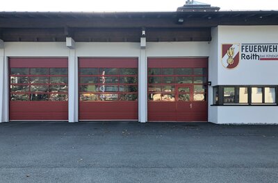 Feuerwehr Reith <p>Das Feuerwehrgebäude in Reith mit drei roten Toren und einem klaren Himmel.</p>