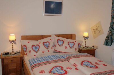 Schlafzimmer Ein gemütliches Schlafzimmer mit einem Doppelbett und Bettwäsche in Herzdesign. An den Nachttischen stehen kleine Lampen, und an der Wand hängt ein Bild.