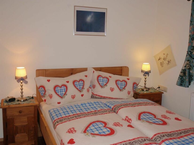 Ein gemütliches Schlafzimmer mit einem Doppelbett und Bettwäsche in Herzdesign. An den Nachttischen stehen kleine Lampen, und an der Wand hängt ein Bild.