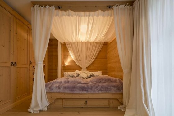 Himmelbett aus hellem Holz mit weißen Vorhängen in einer holzgetäfelten Nische.