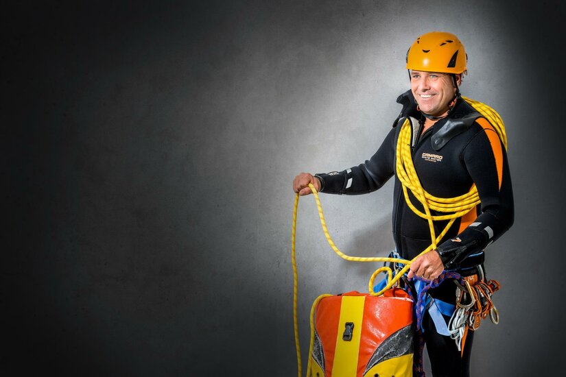 Markus Noichl Ein Kletterer steht mit einem Seil und einer Sicherheitsausrüstung. Er trägt einen Helm und lächelt, bereit für das Klettern.