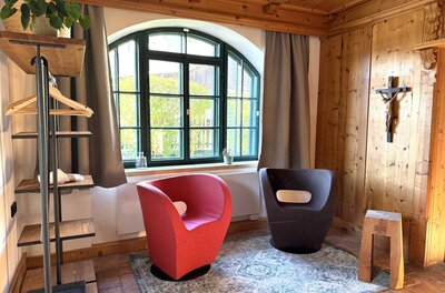 IMG_4745 Ein gemütlicher Raum mit zwei modernen Sesseln in Rot und Schwarz. Ein großes Fenster sorgt für viel Licht und ein Holzregal ergänzt die stilvolle Einrichtung.