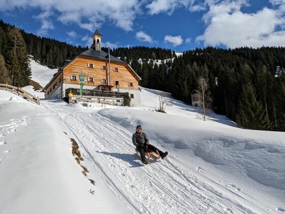 Rodeln bei der Kelchalm Person fährt auf einem Holzschlitten eine verschneite Bahn vor der Kelchalm hinunter.