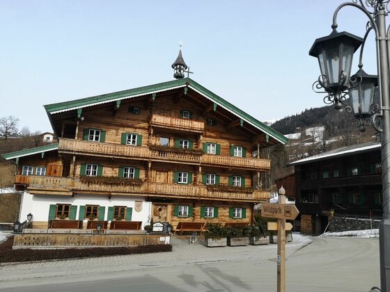 Alpines Holzhaus an der Sonnbergrunde Mehrstöckiges Holzhaus im alpinen Stil mit grünen Fensterläden und Balkonen vor einem bewaldeten Hang.