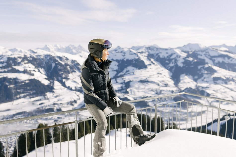 Eine Dame sitzt auf dem Zaun am Berg und genießt die Sonne mit Panoramablick im Hintergrund