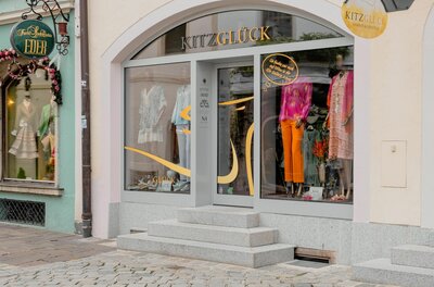 Eingangsbereich des Modegeschäfts Kitzglück mit Schaufenstern und Steinstufen.