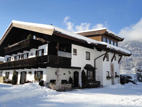 Alpines Landhaus mit weißer Fassade, dunklen Holzbalkonen und schneebedecktem Dach unter blauem Himmel.