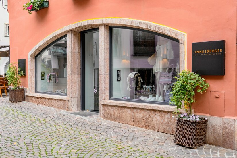 Außenansicht des Sinnesberger Fashionstores mit Schaufenstern in einer gepflasterten Gasse.