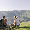 Familie sitzt auf einer Wiese und genießt die Bergsicht mit Blumen in der Hand in Kitzbühel.