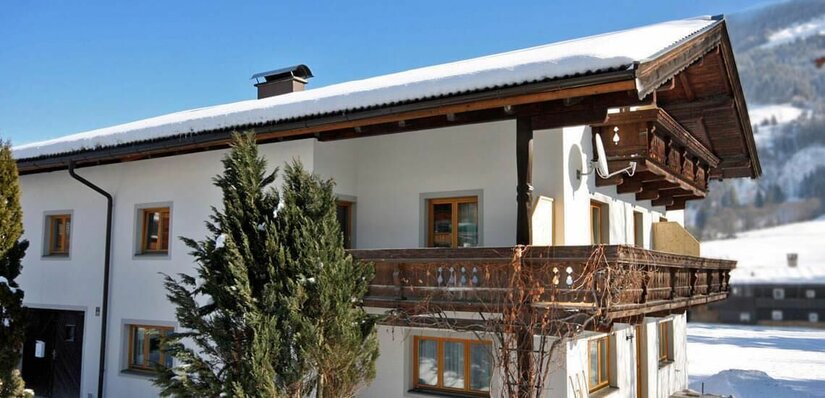 Gästehaus Jochberg im Winter Zweistöckiges weißes Gästehaus mit Holzbalkonen und schneebedecktem Dach in einer Winterlandschaft.