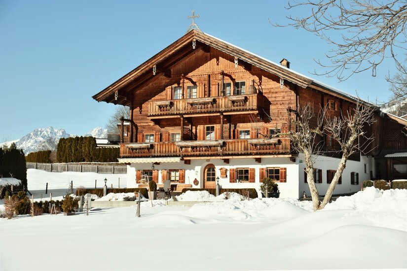 Winter aussen Astlingerhof Ein traditionelles Holzhaus mit Balkonen in einer verschneiten Winterlandschaft vor Bergen.