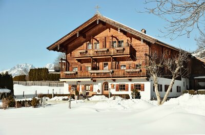 Winter aussen Astlingerhof Ein traditionelles Holzhaus mit Balkonen in einer verschneiten Winterlandschaft vor Bergen.