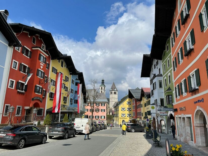 Ortszentrum von Kitzbühel Blick durch eine Straße mit bunten Häuserfassaden auf einen Kirchturm in Kitzbühel.