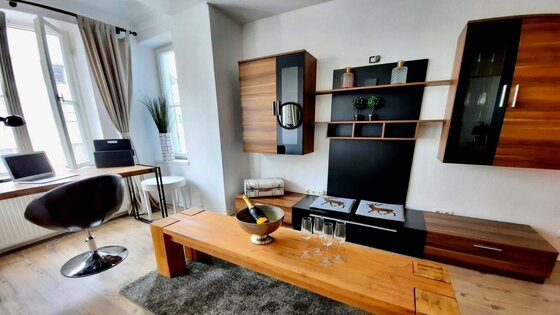 Wohnzimmer Belle Kitz Pure Modernes Wohnzimmer mit Holzmöbeln, Schreibtisch am Fenster und Sektkühler auf dem Couchtisch.
