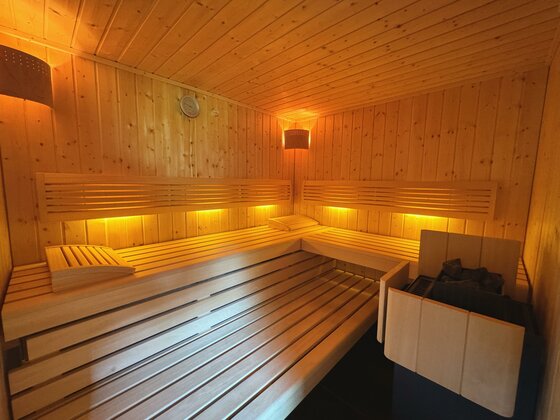 Eine gemütliche Sauna mit Holzinterieur und sanfter Beleuchtung. Die Bänke sind bereit zum Entspannen und Wohlfühlen.