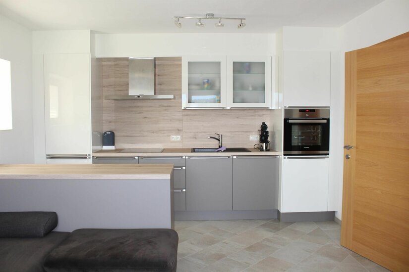 Moderne Küchenzeile in Ferienwohnung Moderne Einbauküche mit grauen Fronten, Holzrückwand, Backofen und Kochinsel.