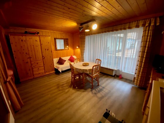 Rustikaler Essbereich mit Holztisch, Stühlen, Schrank und holzverkleideten Wänden.