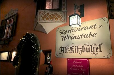 Außenansicht des Restaurants Alt-Kitzbühel mit beleuchtetem Schild, Laterne und dekoriertem Eingang bei Nacht.