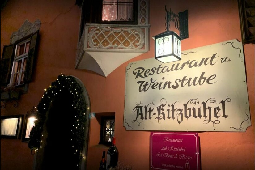 Außenansicht des Restaurants Alt-Kitzbühel mit beleuchtetem Schild, Laterne und dekoriertem Eingang bei Nacht.