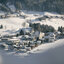 Winterlandschaft in Jochberg bei Kitzbühel mit Dorf, Bergen und Nadelbäumen.