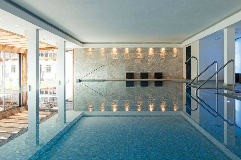 Hallenbad im Kitzhof Resort Modernes Hallenbad mit Natursteinwand, Metallgeländern und blauem Mosaikbecken.