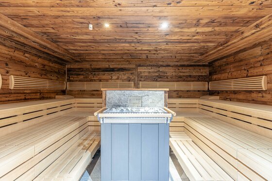 Sauna im Dorfresort Kitzbühel Innenansicht einer Sauna mit Holzwänden, mehrstufigen Sitzbänken und zentralem Saunaofen.