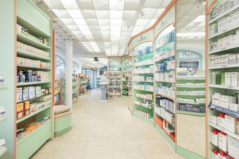 Innenansicht einer hellen Apotheke mit grünen Regalen und zahlreichen Pflegeprodukten.