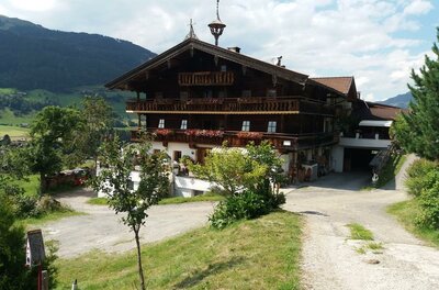 Talhof im Sommer Großes, mehrstöckiges Holzhaus im alpinen Stil mit Blumenbalkonen vor bewaldeten Bergen.
