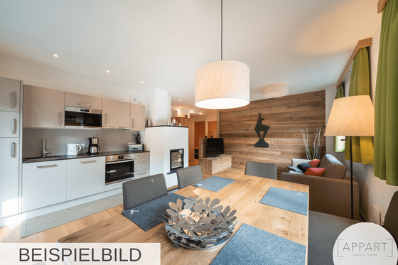 Wohnbereich Alpin Residenzen Eichenheim Moderner Wohn- und Essbereich mit Küchenzeile, Holztisch und Sofa vor einer Wand in Holzoptik.