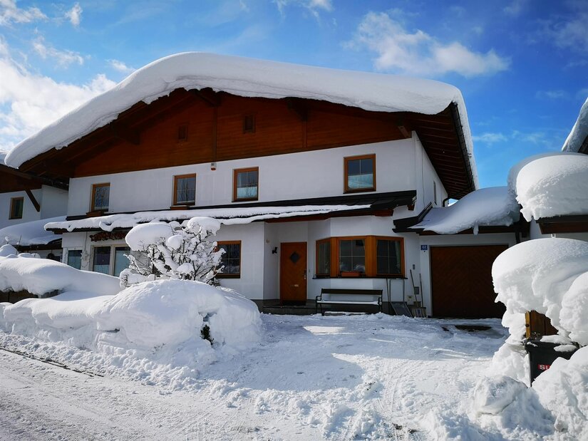 Zweistöckiges Wohnhaus mit holzverkleidetem Giebel und einer dicken Schneeschicht auf dem Dach.