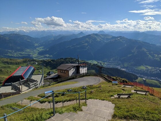 Bergstation am Kitz Trail Blick von einer Bergstation auf Wanderwege, Holzhütten und ein weites Gebirgspanorama unter blauem Himmel.