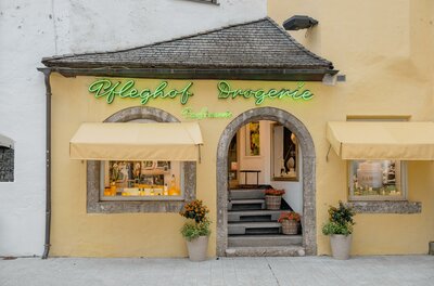 Pfleghof Drogerie Fassade Fassade der Pfleghof Drogerie mit gelber Wand, grüner Leuchtschrift und Rundbogen-Eingang.