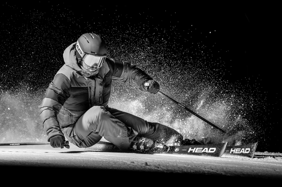 Klabacher Ein Skifahrer fährt in der Nacht auf einer schneebedeckten Piste. Der Schnee spritzt um ihn herum und es herrscht eine dynamische Atmosphäre.