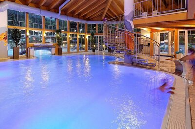 Ein modernes Hallenbad mit leuchtend blauem Wasser und einer Rutsche. Große Fenster sorgen für viel Tageslicht und eine entspannende Atmosphäre.