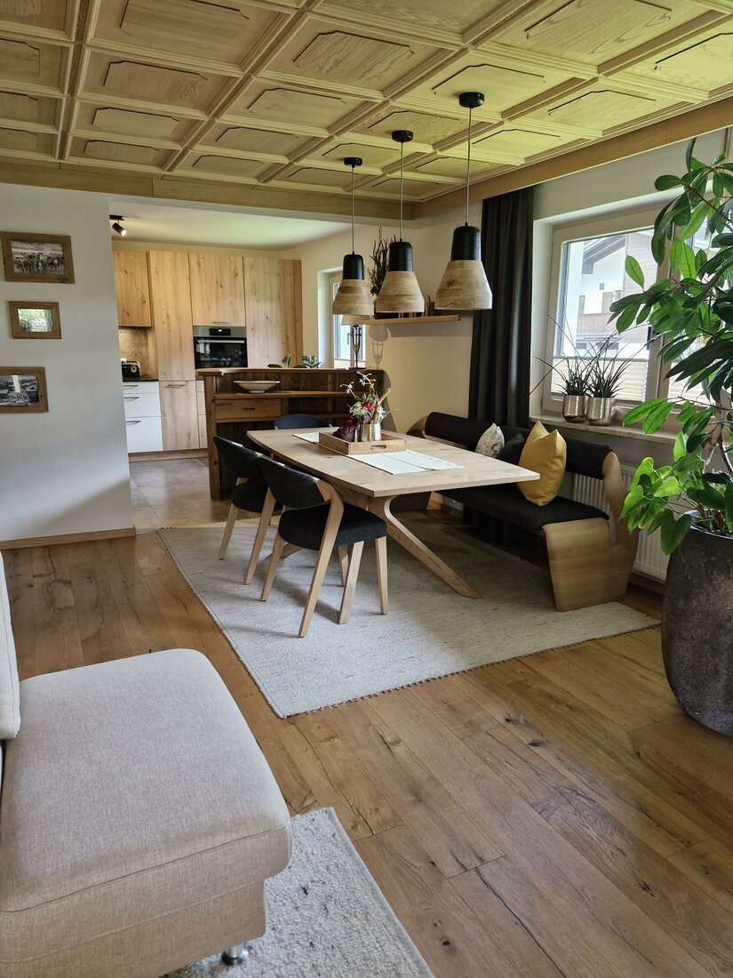Wohnraum Haus Egger Moderner Essbereich mit Holztisch, Sitzbank und Stühlen unter einer Kassettendecke aus Holz.
