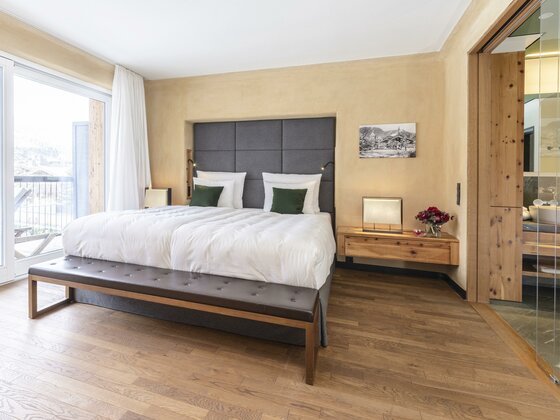 Modernes Hotelzimmer mit Doppelbett, gepolstertem Kopfteil, Parkettboden und Blick ins angrenzende Badezimmer.