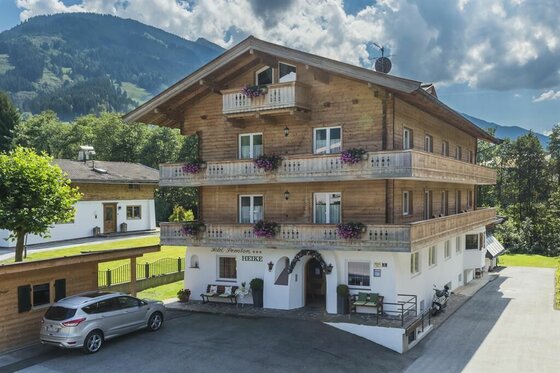 Mehrstöckiges Holzgebäude der Hotel-Pension Heike vor bewaldeten Bergen.