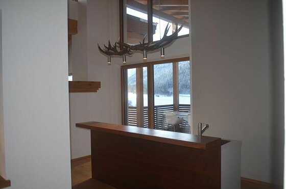 Küche im Apartment Hofer Moderner Tresen aus dunklem Holz mit einer Geweih-Leuchte vor einem Fenster mit Bergblick.
