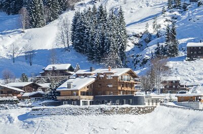 KitzChalet Jochberg im Winter Mehrstöckiges Holzchalet mit schneebedecktem Dach in einer alpinen Winterlandschaft vor bewaldetem Hang.