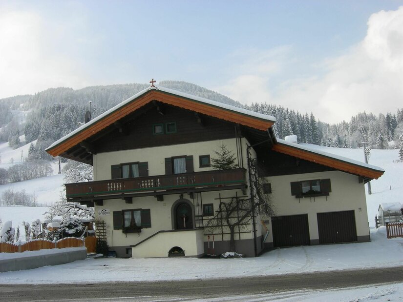 Bergschmied Hausansicht im Winter Zweistöckiges Alpenhaus mit Holzbalkon und Satteldach in einer verschneiten Berglandschaft.