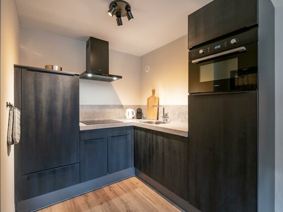 Moderne dunkle Küchenzeile über Eck mit Backofen, Kochfeld und Spüle in einem Appartement.