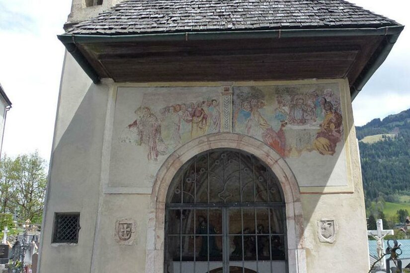Totenleuchte Eine kleine Kapelle mit einem schrägen Dach und einem Gittertor. An der Fassade sind alte Fresken sichtbar.