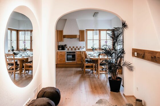Innenansicht Residenz am Berg 4 Blick durch einen Rundbogen in eine Küche mit Holzeinrichtung, Esstisch und einem großen runden Spiegel im Vordergrund.