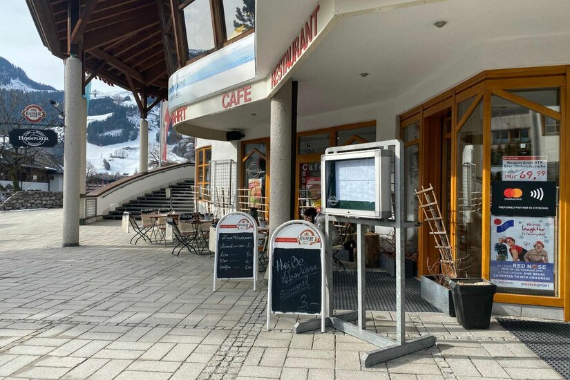 Hornplatzl Sommer Außenansicht des Restaurants Hornplatzl mit Terrasse, Speisekartenaushängen und Blick auf verschneite Berge.
