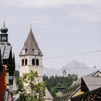 Ein malerischer Blick auf eine Stadt mit einem markanten Kirchturm und bunten Gebäuden im Vordergrund.