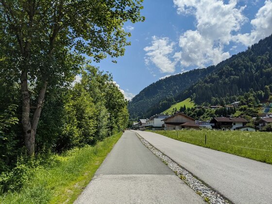 Radweg bei Malerndörfl Asphaltierter Rad- und Gehweg neben einer Straße vor bewaldeten Bergen und Häusern.