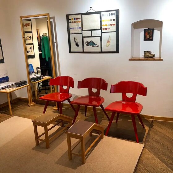 Drei rote Holzstühle und zwei Fußbänke in einem Verkaufsraum mit Schuhgrafiken an der Wand.